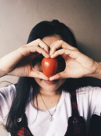 Close-up of woman holding tomato against wall