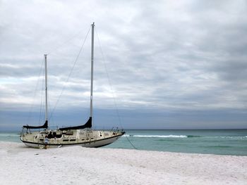 Sailboat at beach against cloudy sky