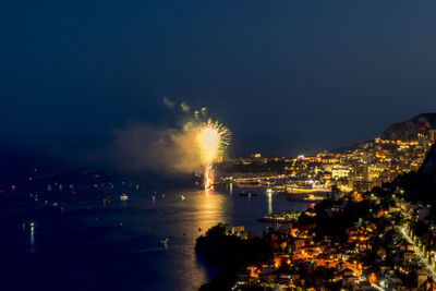 Illuminated city by sea against sky at night