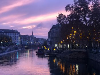 Illuminated bridge over river in city against sky at sunset