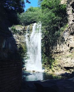 Scenic view of waterfall in forest against sky