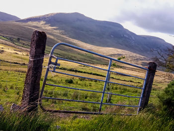 Fence on field by mountains against sky