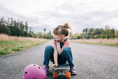 Portrait of a young girl sat on a skateboard thinking