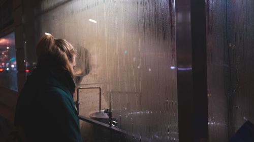 Rear view of woman looking through glass window at night