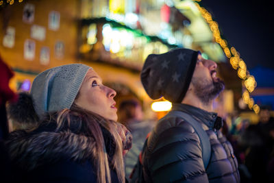 Close-up of couple looking up while standing against illuminated building