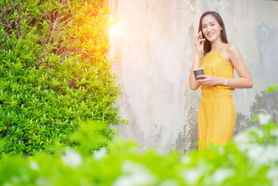 Full length of young woman using phone while standing on plants