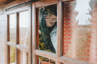 Woman covering face with hand seen through window