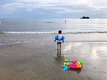 Rear view of boy wearing water wings while walking towards shore at beach