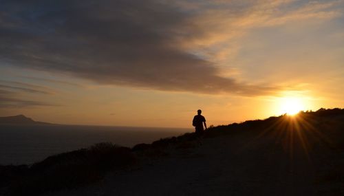 Silhouette man standing on shore against sky during sunset