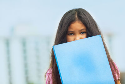 Portrait of girl holding book against blue sky