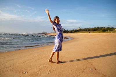 Side view portrait happy woman waving while standing at beach