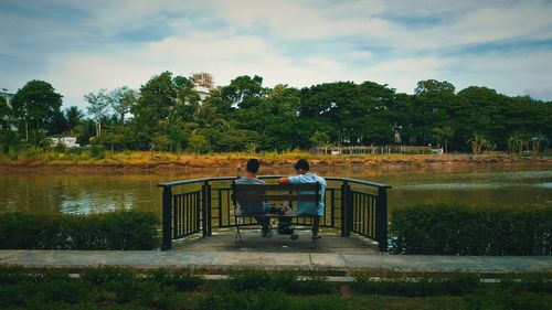 Rear view of friends sitting on bench by lake