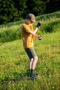 Side view of young man holding rope while standing on grassy field at park during sunset