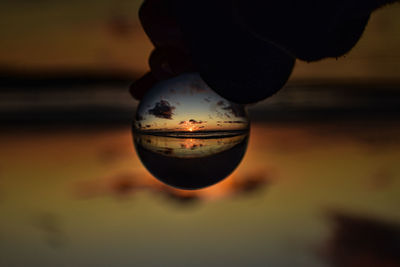 Close-up of person holding candle against sky during sunset