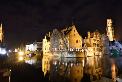 Illuminated buildings by river against sky at night