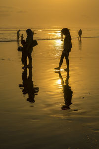 Silhouette people on beach against sky during sunset