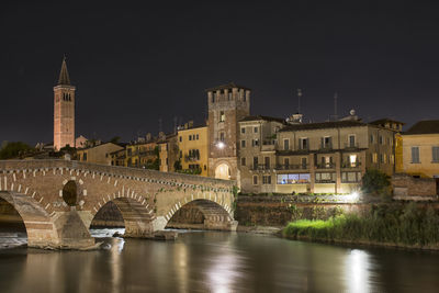 Bridge over river by buildings against sky at night