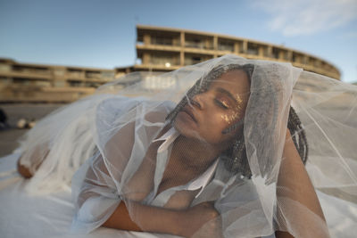 Young woman in tulle netting lying outdoors