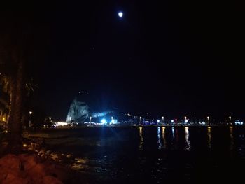 Illuminated city by river against sky at night