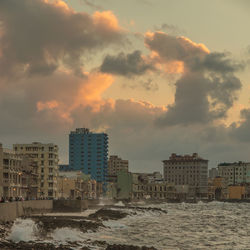 Sea by cityscape against sky during sunset