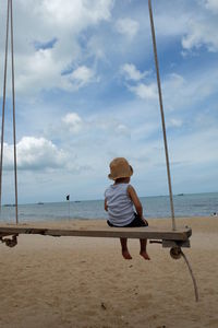 Rear view of boy sitting on swing at beach