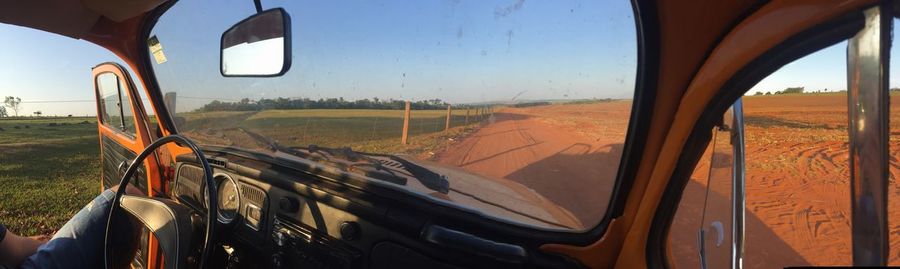 Panoramic view of farm by dirt road seen through windshield