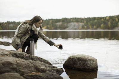 Woman washing thermos at lakeshore