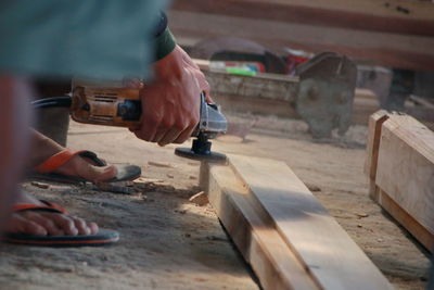 Low section of man holding work tool on plank