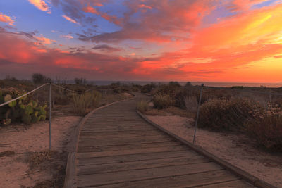 Boardwalk against sky during sunset