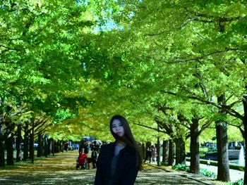 Portrait of woman standing by trees in park