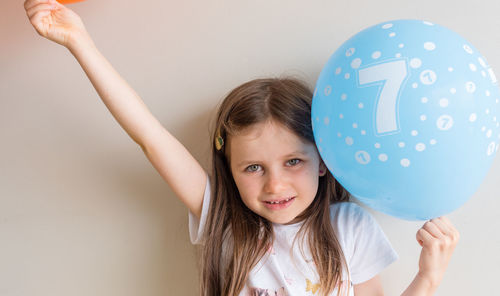 Portrait of cute girl holding blue balloon against wall