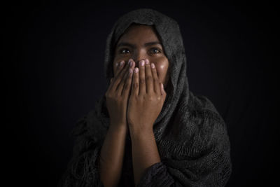 Portrait of woman covering face against black background