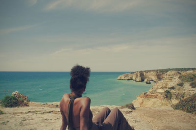 Woman sitting on cliff against sea