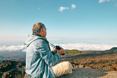 Rear view of man looking through binoculars at panoramic view of summits of active volcano etna