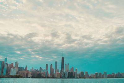 City at waterfront against cloudy sky