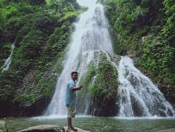 Man standing against waterfall in forest