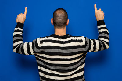 Rear view of man with arms raised against blue background