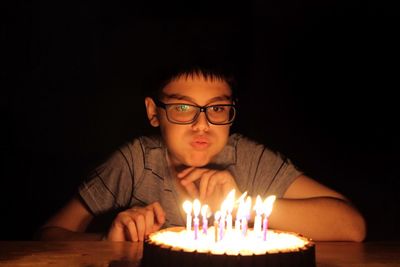 Close-up of boy blowing birthday candles against black background