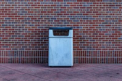 Garbage can on walkway against brick wall