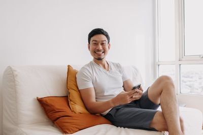 Portrait of young woman using mobile phone while sitting on bed at home