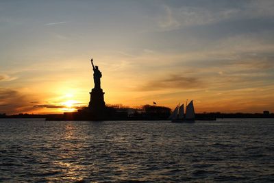 Statue of liberty by hudson river in city during sunset