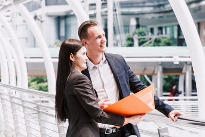 Colleagues discussing while standing on bridge against buildings in city