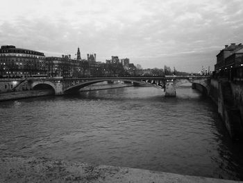 Bridge over river by buildings against sky in city