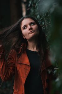 Beautiful young woman looking away while standing against plants