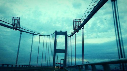 Low angle view of suspension bridge against cloudy sky