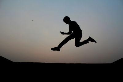 Low angle view of silhouette boy jumping against sky during sunset