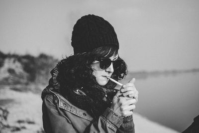 Young woman igniting cigarette against sky