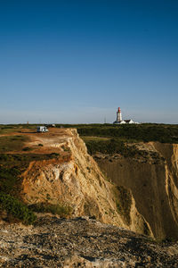 Lighthouse by sea against clear blue sky