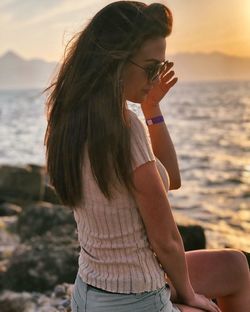 Midsection of woman sitting at beach during sunset