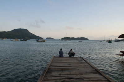 People on pier by sea against sky